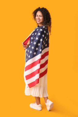 Sarı arka planda Amerikan bayrağı olan genç Afro-Amerikalı kadın.
