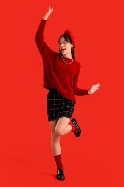 Kırmızı elbiseli, renkli arka planda başarıyı kutlayan şık bir genç kadın.