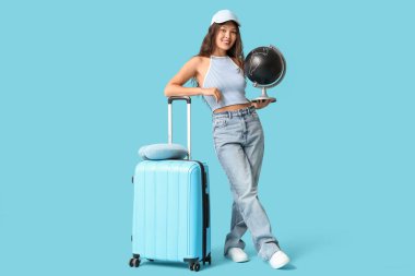 Küre, bavul ve mavi arka planda boyun yastığı olan genç Asyalı kadın. Seyahat kavramı