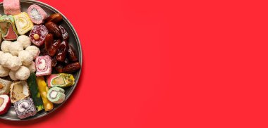 Kırmızı zemin üzerinde farklı lezzetli ikramlardan oluşan tabaklar ve metin için yer. Divaly kutlaması