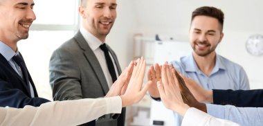 Bir grup iş adamı ofiste el ele tutuşuyor. Birlik kavramı