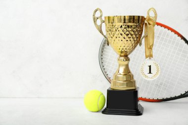 Birincilik madalyası, tenis raketi ve arka planda top olan altın kupa.