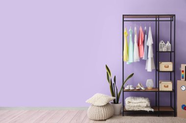 Çocuk elbiseleri ve ayakkabıları olan raf ünitesi odada leylak duvarın yanında.