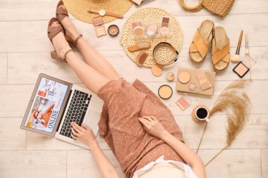 Dizüstü bilgisayarı ve aksesuarları olan bir kadın açık ahşap zeminden alışveriş yapıyor.