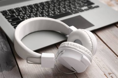 Gri ahşap arka planda dizüstü bilgisayarı olan modern beyaz kulaklıklar