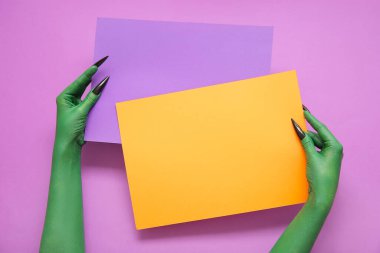 Mor arka planda boş kağıt çarşafları olan cadının yeşil elleri. Cadılar Bayramı