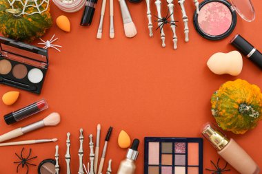 Farklı makyaj ürünlerinden yapılmış çerçeve ve turuncu arka planda Cadılar Bayramı dekoru