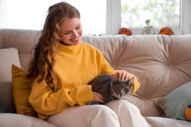 Evdeki kanepede oturan kedisi olan genç bir kadın.
