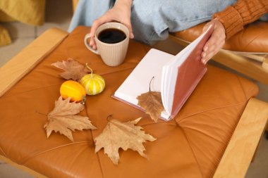 Kitaplı genç bir kadın, bir fincan kahve, sonbahar yaprakları ve balkabakları evde, yakın plan.