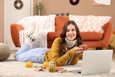 Bir fincan kahve ve dizüstü bilgisayarı olan genç bir kadın sonbahar günü evde yatıyor.