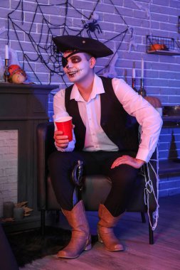 Korsan gibi giyinmiş genç adam Cadılar Bayramı partisinde oturup içki içiyor.