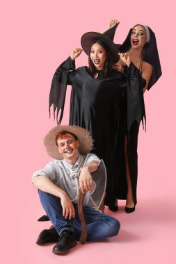 Cadılar Bayramı partisi için pembe arka planda kostümlü genç arkadaşlar.