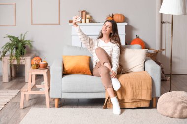 Cep telefonlu genç bir kadın evdeki kanepede selfie çekiyor.