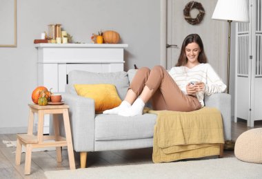 Evdeki koltukta cep telefonu kullanan genç bir kadın.