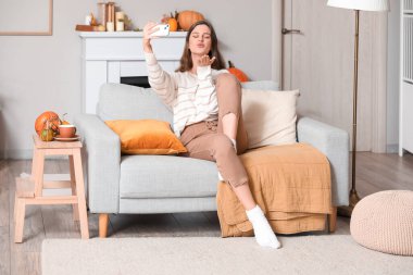 Cep telefonlu genç bir kadın evdeki kanepede selfie çekiyor.