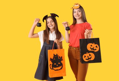 Cadılar Bayramı için annesiyle birlikte giyinmiş küçük bir kız. Kazanlar ve sarı arka planda hediye çantaları var.