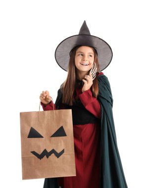 Cadılar Bayramı için cadı gibi giyinmiş küçük bir kız hediye çantası ve beyaz arka planda iskelet eli.