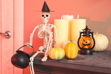 Skeleton with Halloween pumpkins and candles on mantelpiece in hall, closeup clipart