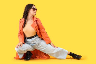 Sarı arka planda oturan sonbahar elbiseli şık Asyalı kadın.