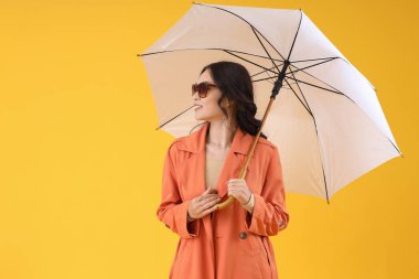 Sarı arka planda şemsiyesi olan sonbahar elbiseli şık Asyalı bir kadın.