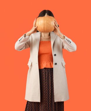 Kırmızı arka planda balkabağı olan sonbahar elbiseli şık genç bir kadın.