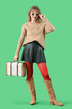 Yeşil arka planda sonbahar kıyafetleri içinde şık genç bir kadın.