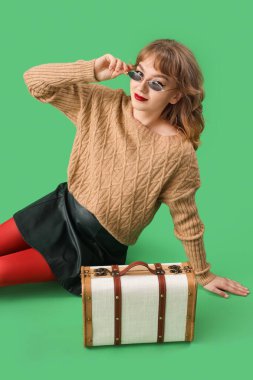 Yeşil arka planda oturan sonbahar elbiseli şık genç kadın.