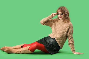 Yeşil arka planda oturan sonbahar elbiseli şık genç kadın.