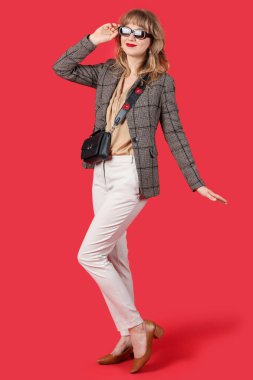 Kırmızı arka planda sonbahar kıyafetleri içinde şık bir genç kadın.