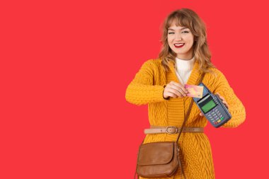 Kırmızı arka planda kredi kartı ve ödeme terminali olan şık genç bir kadın.