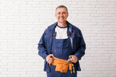 Beyaz tuğla arka planda alet kemeri olan erkek tamircinin portresi