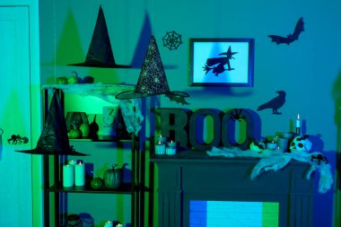 Cadılar Bayramı için dekore edilmiş karanlık oturma odasının içinde raf ünitesi ve şömine rafı var.