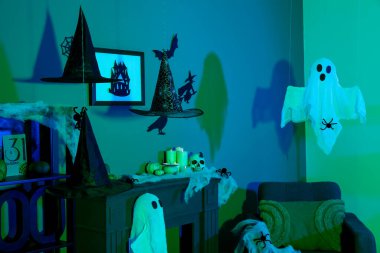 Cadılar Bayramı için dekore edilmiş karanlık oturma odasının içinde koltuk ve şömine rafı var.