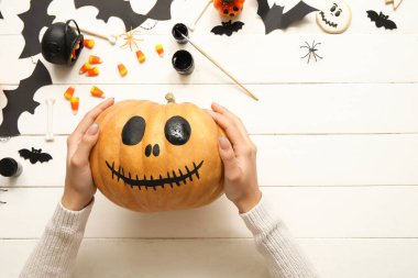 Beyaz ahşap masada boyanmış Cadılar Bayramı kabağı olan kadın.