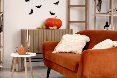 Cadılar Bayramı için dekore edilmiş oturma odasının içinde kırmızı kanepe ve masa var.