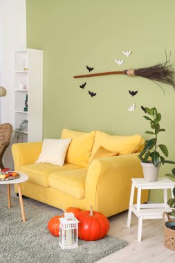 Cadılar Bayramı için sarı kanepe ve cadı süpürgesiyle dekore edilmiş oturma odasının içi.