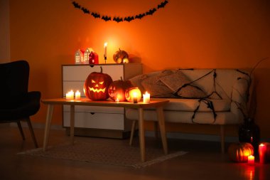 Cadılar Bayramı balkabakları ve yanan mumlarla dolu karanlık oturma odasının içinde.