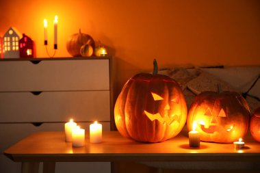 Halloween pumpkins with burning candles on table in dark living room clipart