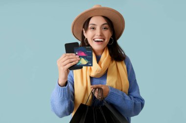 Alışveriş çantaları, kredi kartları ve mavi arka planda cep telefonu olan genç kadın.