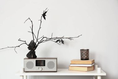 Table with books, tree branches and radio near white wall clipart