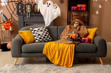 Sonbahar kıyafetleri içinde korkunç Cadılar Bayramı iskeleti hediye kutusu ve oturma odasındaki kanepede oturan tarantula.