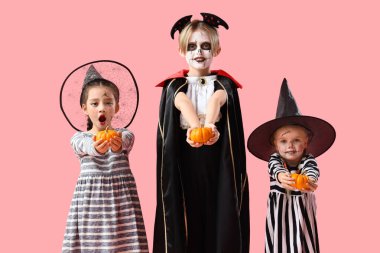 Cadılar Bayramı için giyinmiş küçük çocuklar ve pembe arka planda balkabakları.