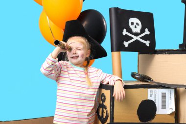 Cadılar Bayramı 'nda korsan gibi giyinmiş, mavi arka planda karton gemi olan küçük bir kız.