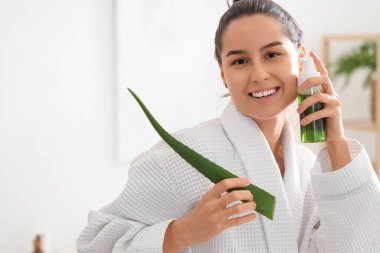 Bornozlu, aloe veralı ve evinde bir şişe kozmetik ürünü olan genç ve güzel bir kadın.