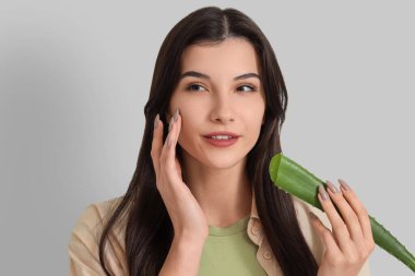 Gri arka planda aloe vera yaprağı olan güzel, genç ve mutlu bir kadın.