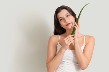 Gri arka planda aloe vera yaprağı olan güzel genç bir kadın.