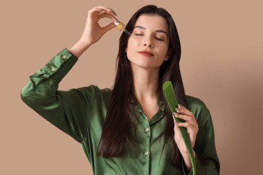 Aloe vera yaprağı ve bej arkaplanda pipeti olan güzel bir genç kadın.