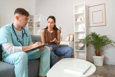 Erkek doktor evde hasta genç bayanı dinliyor.