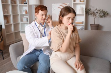 Erkek doktor evde genç bir kadının ciğerlerini dinliyor.