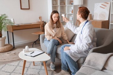 Erkek doktor, evdeki genç kadının ateşini ölçüyor.